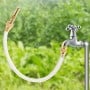 Lance d'arrosage en aluminium avec flexible transparent fixée à un robinet dans un jardin flou