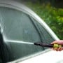 Lance d'arrosage tenue par une main jaillissant un jet d'eau sur une vitre de voiture