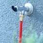 Robinet extérieur en métal avec raccord en laiton et tuyau d'arrosage rouge fixé sur un mur texturé bleu.