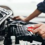 Main tenant une pince crocodile rouge sur un composant moteur de voiture