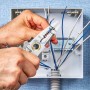 Pince à dénuder utilisée pour préparer un câble électrique dans un tableau de distribution.