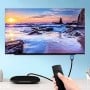 شاشة تلفاز تعرض منظر غروب الشمس فوق البحر، متصلة بجهاز بواسطة كابل HDMI مع يد تحمل جهاز تحكم عن بعد