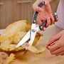 Main tenant des ciseaux à volaille en train de couper la patte d'un poulet rôti sur une surface en bois.