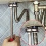 Clé sanitaire avec manche rouge utilisée sous un lavabo pour serrer une tuyauterie chromée flexible.