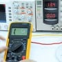 Multimètre digital jaune DT9205A affichant une lecture sur écran LCD, placé devant un équipement de test électronique.