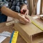 Personne mesurant et marquant une planche en bois avec un mètre ruban et un crayon sur un établi.
