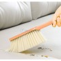 Brosse de lavage rose utilisée pour nettoyer des miettes sur un canapé beige