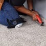 Personne agenouillée sur un tapis avec genouillères à coque rigide en PVC en train de couper un plinthage.