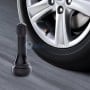 Valve noire de gonflage posée devant une roue de voiture en aluminium, valve en cuivre visible sur le pneu.