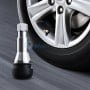 Valve de pneu chromée avec base en caoutchouc posée devant une roue de voiture